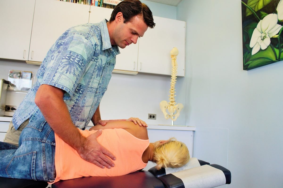 Dr. Tyler Ryan performing a chiropractic adjustment on a patient beside a spine model at the clinic