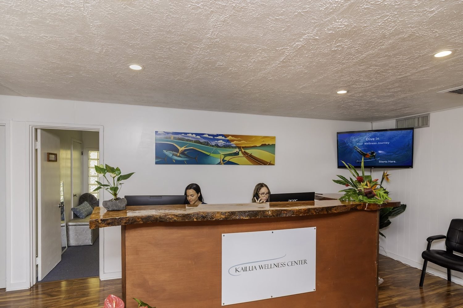 The warm front-desk reception at Kailua Wellness Center, with staff, wood millwork and ocean artwork on the wall
